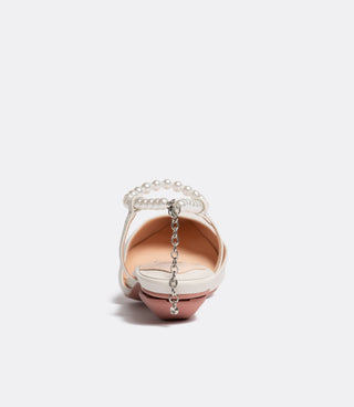 Back view of a white flat shoe with a pearl strap and a dangling silver chain charm on a pink heel