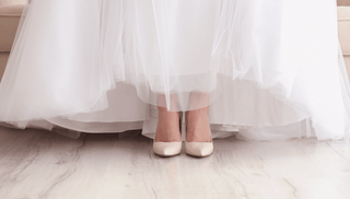 Ivory satin high-heeled wedding shoes peeking from beneath a tulle bridal gown