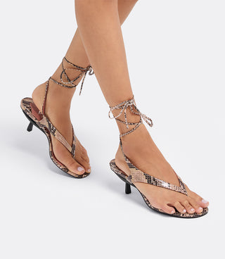 Model wearing the VICE VERSA Margo Sandals in snake print with ankle ties, one in heel mode and one folded flat