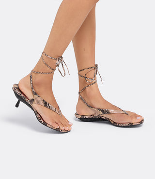 Model walking in the VICE VERSA Margo Sandals in snake print with wrap-around ankle ties