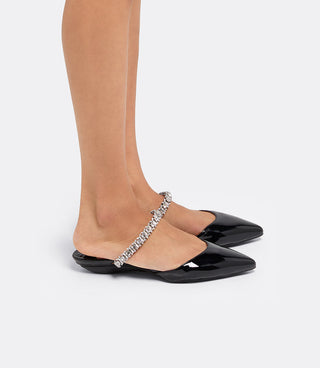 Model wearing the VICE VERSA Isadora Mules in black patent folded into flats