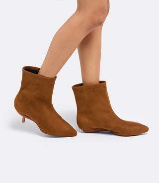 Model walking in the VICE VERSA Bowery Boot in walnut faux suede ankle boots, one in heel mode and one folded flat