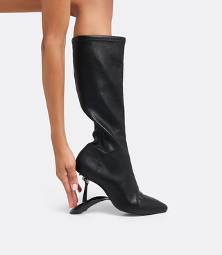Model folding the heel of the VICE VERSA Knee High Boots in black faux leather to convert it to a flat