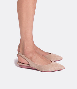 A pair of pointed-toe slingback flats in light beige suede with a pink sole, shown on a model's feet against a light gray background.