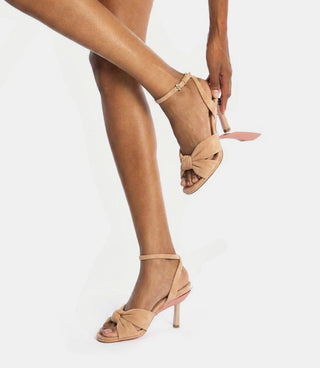 Beige high-heeled sandals worn by a person on a white background
