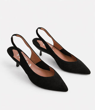 Pair of black suede slingback heels on a light gray background