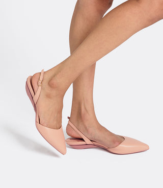 A pair of women's pointed-toe slingback flats in a light blush pink leather, shown on a model's feet against a clean light gray studio background.