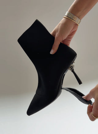 Black high-heeled boot held by a hand against a neutral background