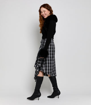 VICE VERSA founder smiling in the Knee High Boots in black faux leather, styled with a plaid asymmetric skirt and black top with faux fur trim