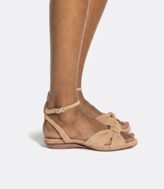 Tan suede sandals with a knot detail worn by a person on a white background