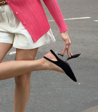 Person wearing black pointed-toe shoes on a street.