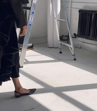 Person wearing black slingback flat shoes standing near a metal ladder in a sunlit room